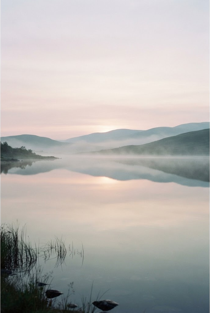 A calm lake at dawn with soft mist.