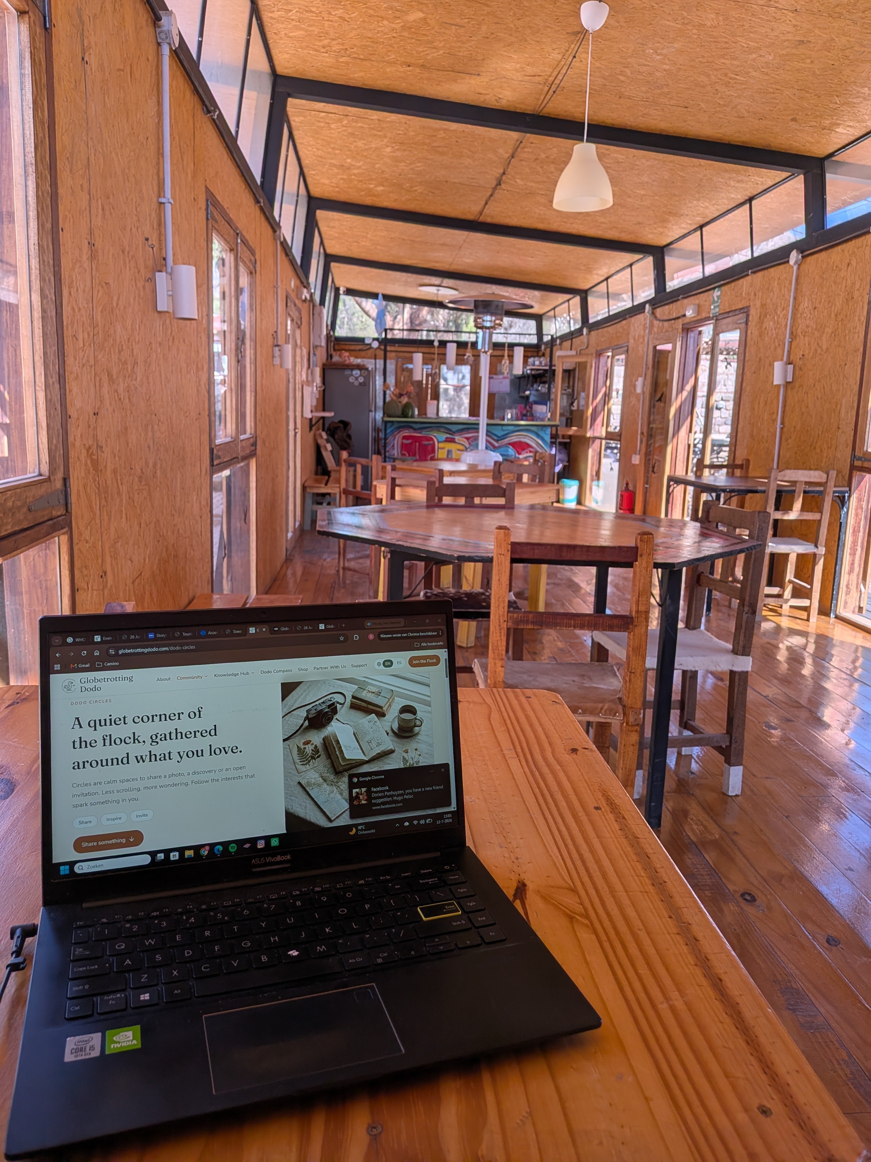 A laptop open on a wooden table in a hostel common room, showing the Globetrotting Dodo website.